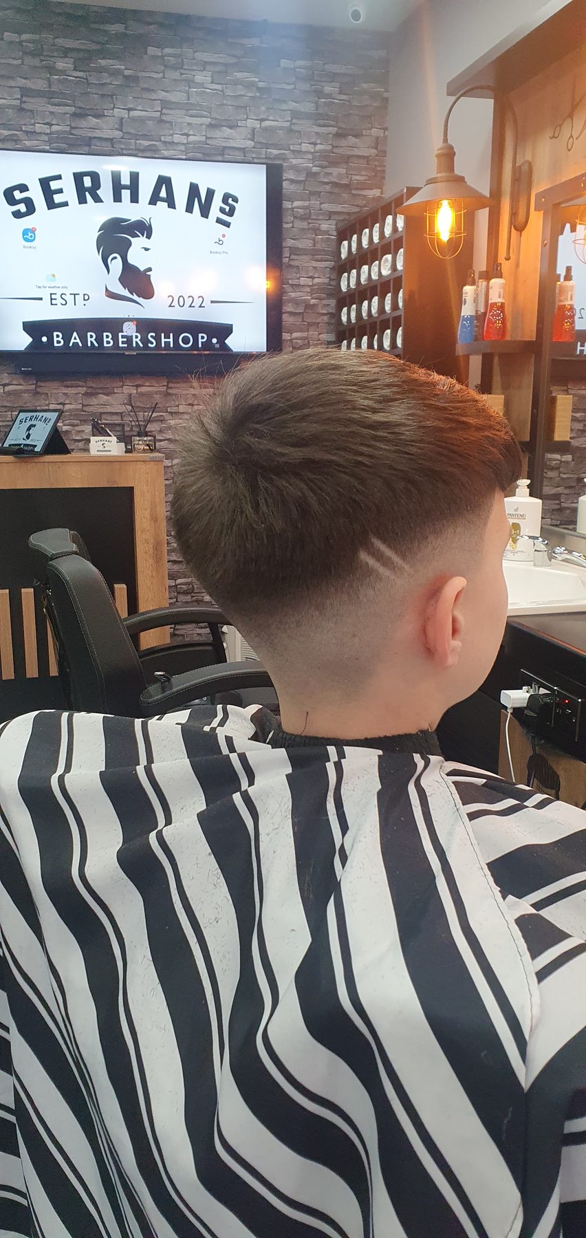 A fade with a shaved line, the shop logo on the screen behind