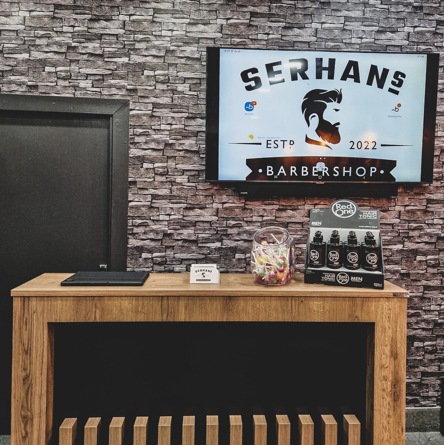 The reception desk with the Serhans Barbershop logo on the screen