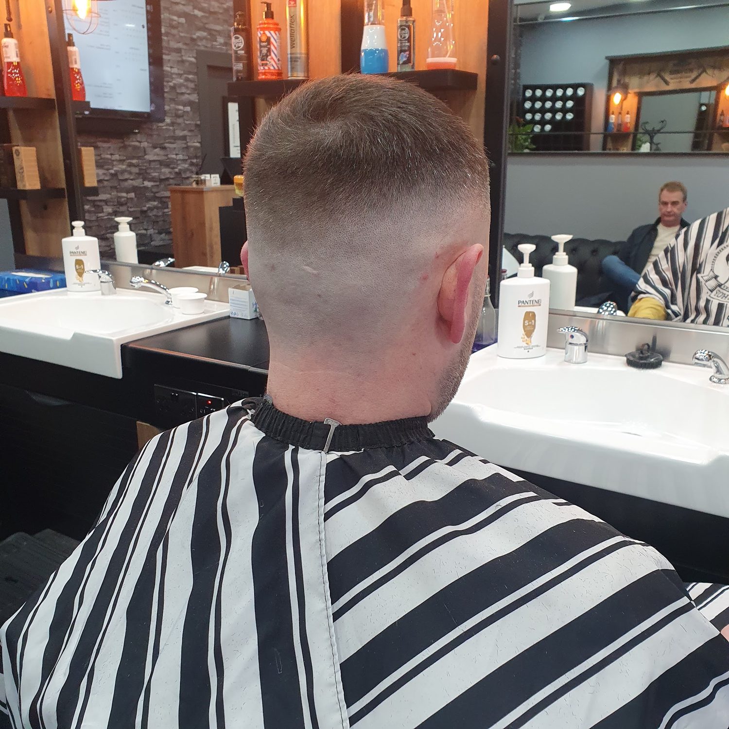 A skin fade from behind, the client in a striped cape